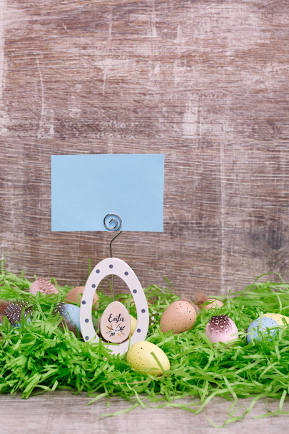 Easter greeting card and colorful quail eggs on a green grass in front of a wooden background. Copy space for the text. - Фото, зображення