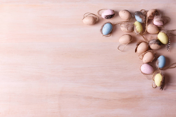 Top view of a heap of colorful quail eggs with feathers on a light wooden background with copy space for text. Easter holidays concept. - Foto, afbeelding