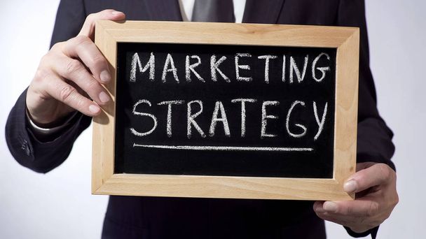 Marketing strategy written on blackboard, businessman holding sign, business - Foto, imagen