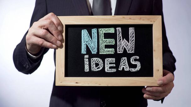 New ideas written on blackboard, male holding business concept sign, motivation - 写真・画像