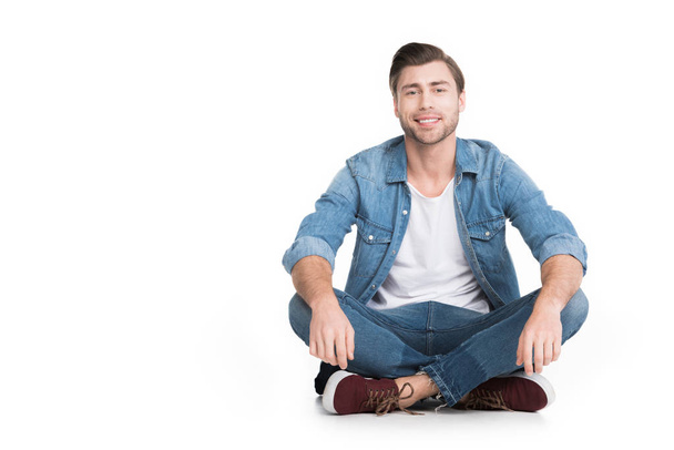 young smiling man sitting in jeans looking at camera, isolated on white - Fotoğraf, Görsel