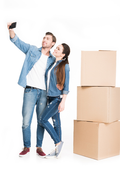 couple taking selfie on smartphone with moving boxes behind, isolated on white - Photo, Image