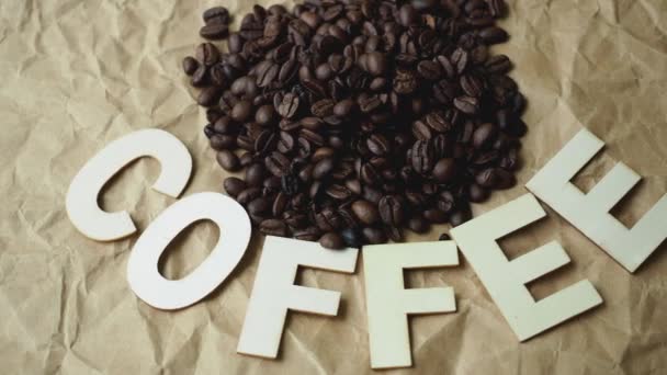 Φρυγμένους κόκκους καφέ σε χαρτί καφέ περιτυλίγματος. Καφέ επιγραφή - Πλάνα, βίντεο