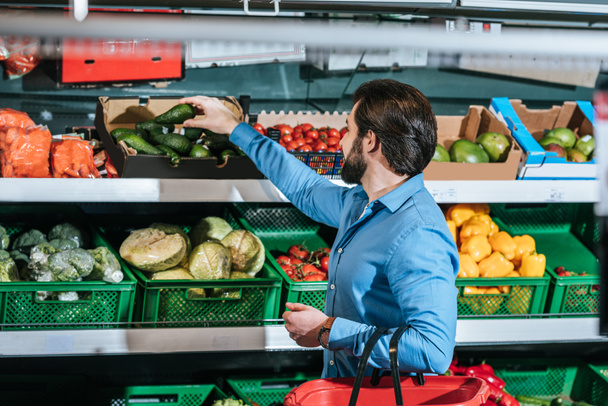 man with shopping basket choosing fresh vegetables in grocery shop - Foto, Bild