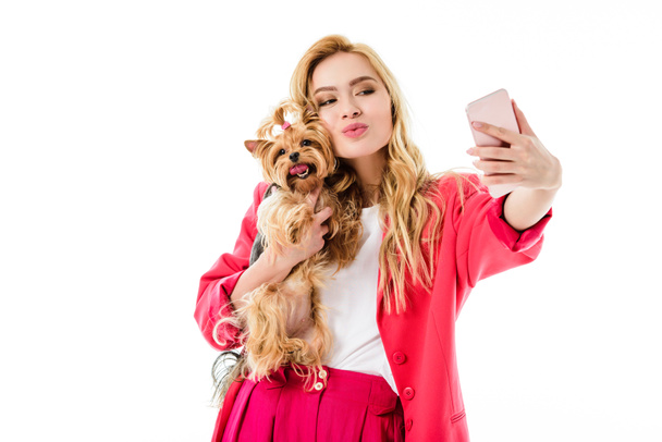 Young girl wearing pink suit holding cute Yorkshire terrier and taking selfie isolated on white - Photo, Image