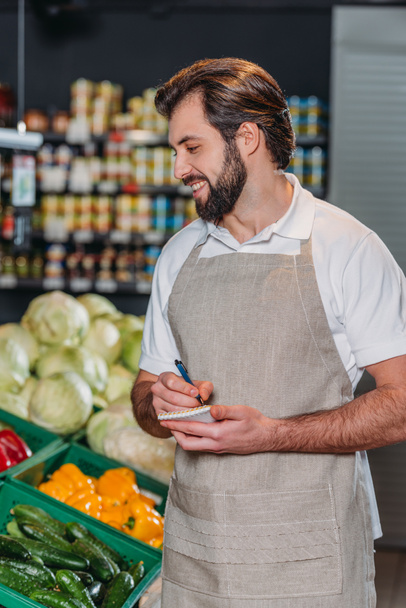 assistente negozio sorridente in grembiule con taccuino in supermercato
 - Foto, immagini