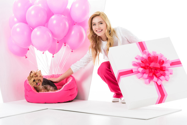 Blonde woman in pink clothes surprised by Yorkshire terrier in gift box isolated on white - Photo, Image