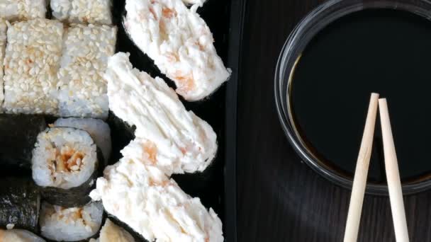 Şık koydu suşi soya sosu ve Çin bambusu yanında siyah bir ahşap zemin üzerine sopa ayarlayın. Somon balığı, yılanbalığı, salatalık karides ve diğer çeşitli doldurma ile çeşitli suşi rulo - Video, Çekim