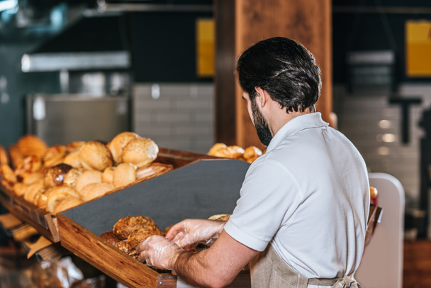 vista trasera del asistente de tienda masculino que organiza pan fresco en el supermercado
 - Foto, Imagen