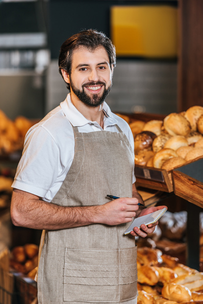 ritratto di sorridente commessa maschile in grembiule con taccuino nel supermercato
 - Foto, immagini