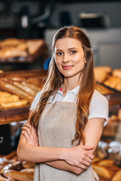 Porträt einer lächelnden Verkäuferin in Schürze, die im Supermarkt in die Kamera blickt - Foto, Bild