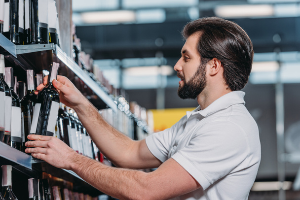 male shop assistant arranging alcohol in supermarket - Fotó, kép