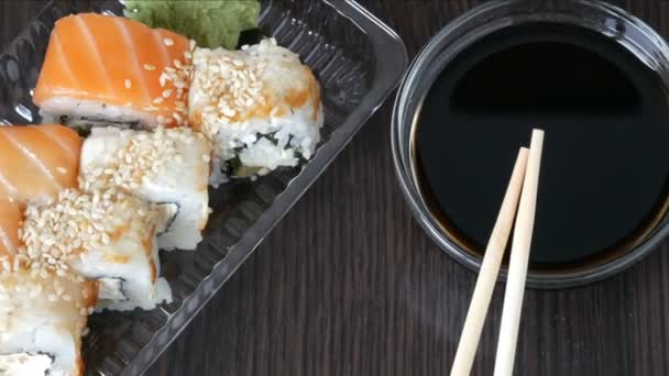 Tyylikkäästi asetetut sushi asetettu musta puinen tausta vieressä soijakastike ja kiinalainen bambu tikkuja. Erilaisia sushi-rullia lohen, ankeriaan, kurkun katkarapujen ja muiden erilaisten täytteiden kanssa
 - Materiaali, video