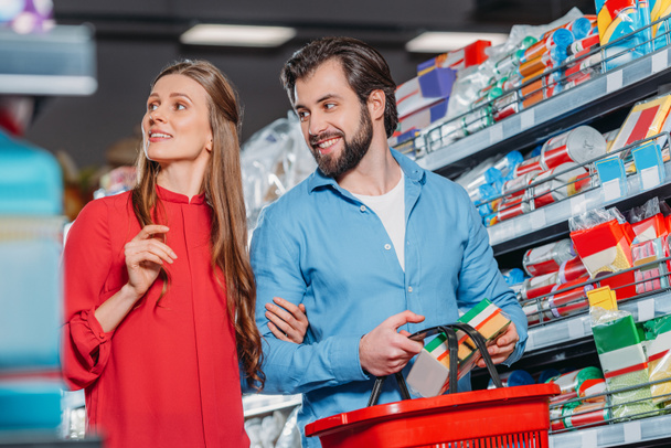 portrait of smiling couple with shopping basket shopping together in supermarket - Foto, imagen