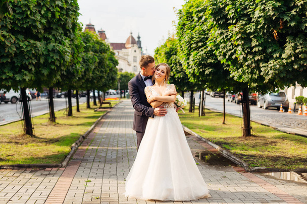the groom gently kisses and embraces a elegant bride against the background of the city - Photo, Image