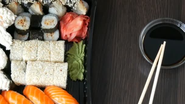 Stylově stanovené sushi na černém pozadí dřevěná vedle sojovou omáčku a čínské bambusové tyče. Různé sushi rohlíky s losos, úhoř, okurka krevety a další různé nádivky - Záběry, video