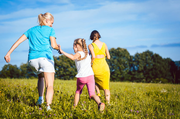 zwei Frauen und Mädchen spielen auf Sommerwiese und rennen  - Foto, Bild