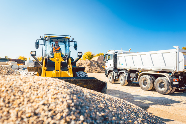 Trabajador de la construcción haciendo obras de tierra con cargador de ruedas y camión de escombros
 - Foto, imagen
