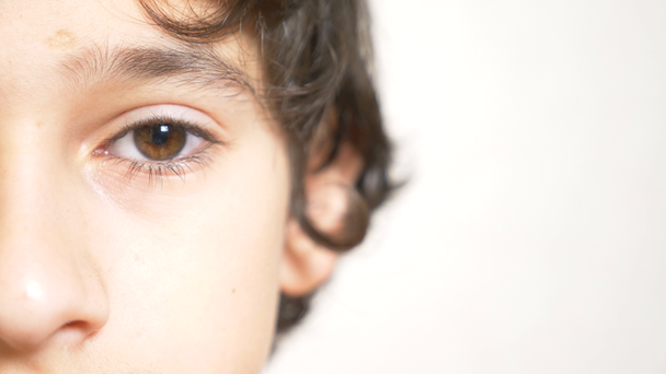 Een jonge jongen kijkt naar de camera. 4 k. close-up, halve gezicht, kopie ruimte. Slow motion - Video