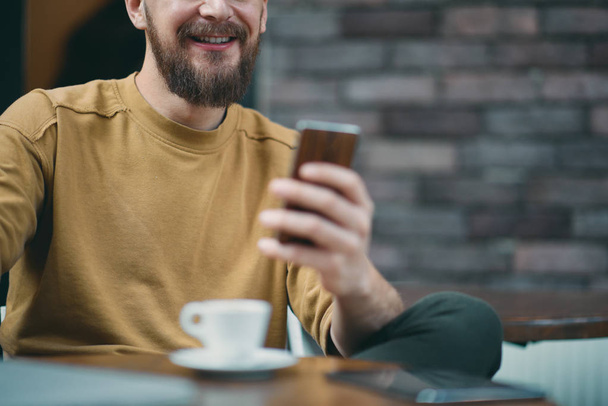 Fiatal ember ül a kávézó, és intelligens telefon használata. - Fotó, kép