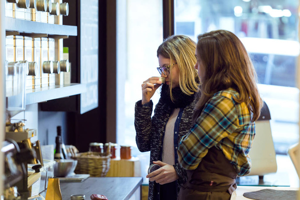 Όμορφη νεαρή γυναίκα μυρίζοντας τσάι φύλλα πωλούνται κατά βάρος σε βιολογικό κατάστημα. - Φωτογραφία, εικόνα
