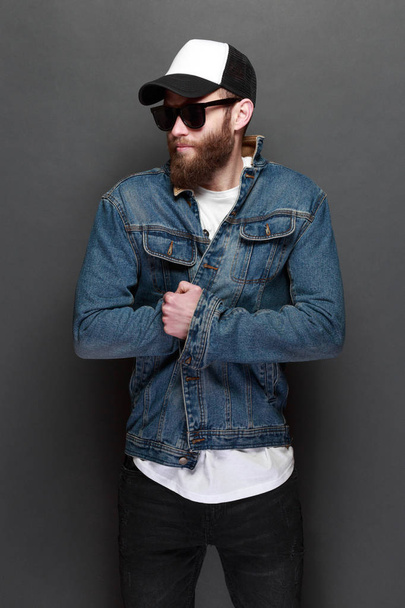 Hipster guapo modelo masculino con barba vistiendo camiseta blanca en blanco y una gorra de béisbol con espacio para su logotipo o diseño en estilo urbano casual - Foto, Imagen
