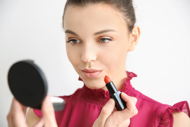 Young woman applying lipstick on light background. Professional makeup products - Foto, imagen