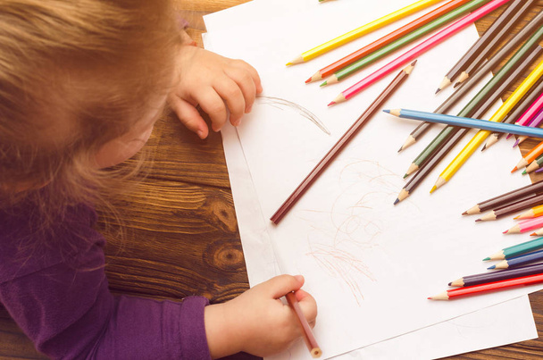 Little girl draws with pencils on a wooden table - Fotó, kép