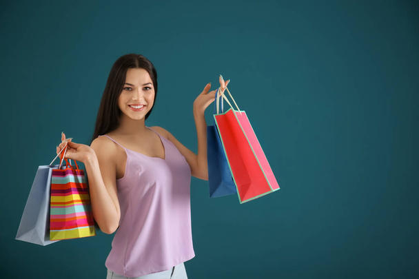 Happy young woman with shopping bags on color background - Photo, image