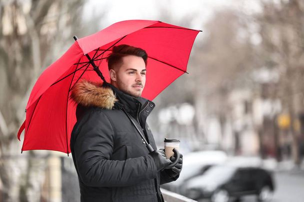 Genç adam açık havada kırmızı şemsiye ile sıcak giysiler - Fotoğraf, Görsel