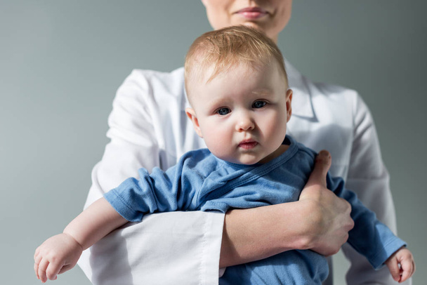 cropped shot of female pediatrician holding beautiful little baby on grey - Photo, Image