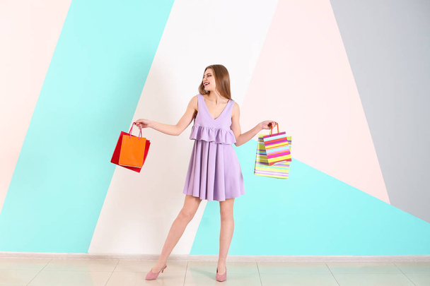Beautiful young woman with shopping bags against color wall - Fotoğraf, Görsel