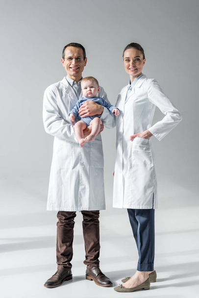 happy adult pediatricians with little baby on grey - Фото, изображение