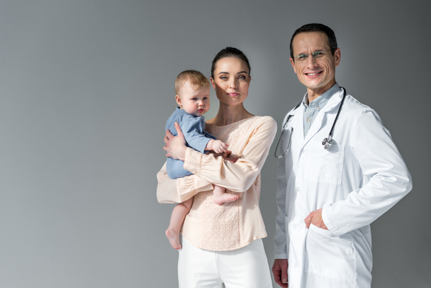 mother and child looking at camera with pediatrician on grey - Foto, Imagem