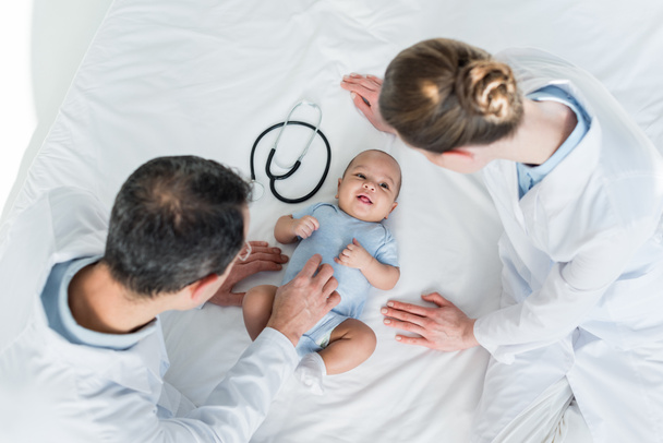 high angle view of pediatricians tickling little baby in bed - Photo, Image