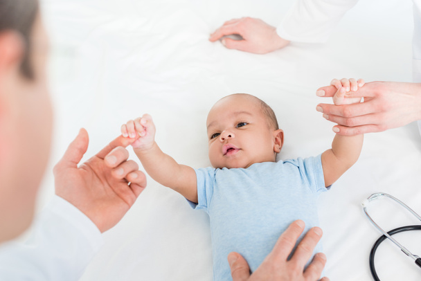 cropped shot of pediatricians tickling adorable little baby on bed - Fotó, kép