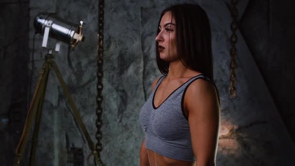 Sexy sporty girl with a beautiful inflated booty and inflated press with dumbbells in the room against the background of a stone gray wall raises her hands with dumbbells for training a bicep. Close - Footage, Video