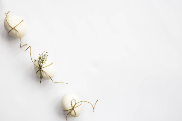 白いミニマルなイースターエッグ麻ひもと線と並ぶ白い背景にカスミソウの花飾られています。イースターのコンセプトです。平面図、平面レイアウト - 写真・画像