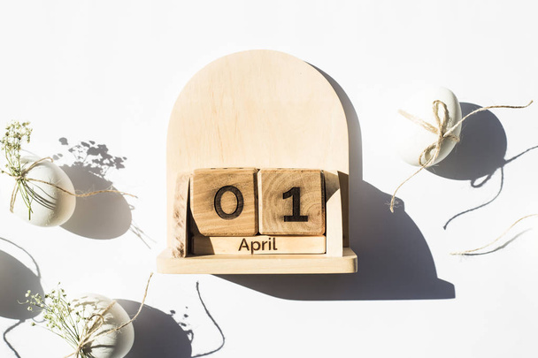 Деревянный календарь - 1 апреля - дата католической Пасхи 2018 года. Рядом с белыми минималистичными пасхальными яйцами. Плоский, вид сверху
 - Фото, изображение