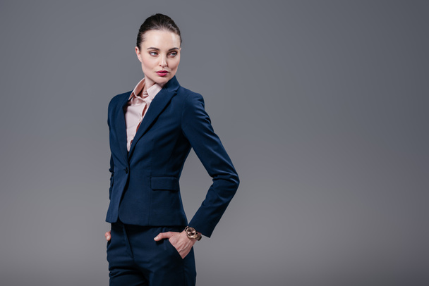 attractive adult businesswoman with hands in pockets looking away isolated on grey - 写真・画像