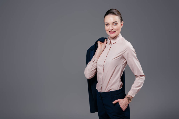 smiling adult businesswoman with jacket on shoulder isolated on grey - Foto, Imagem