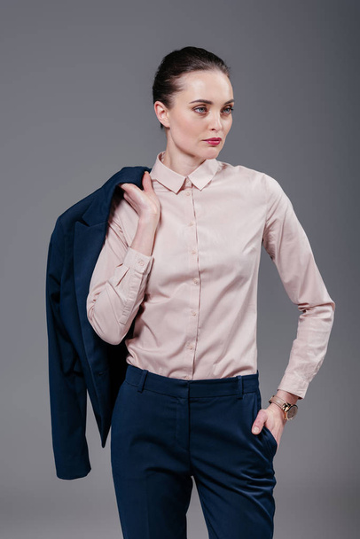 stylish adult businesswoman with jacket on shoulder looking away isolated on grey - Φωτογραφία, εικόνα