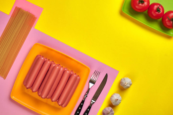 Ковбаски з помідорами, спагетті та часником на жовтому та рожевому мінімальному тлі. Пласка лежала. Вид зверху
. - Фото, зображення