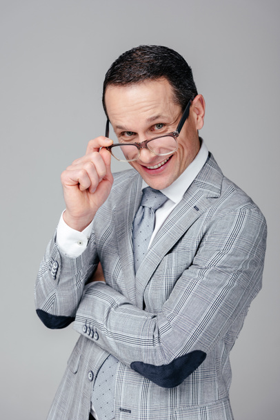 uomo d'affari adulto sorridente guardando la fotocamera sopra gli occhiali isolati su grigio
 - Foto, immagini