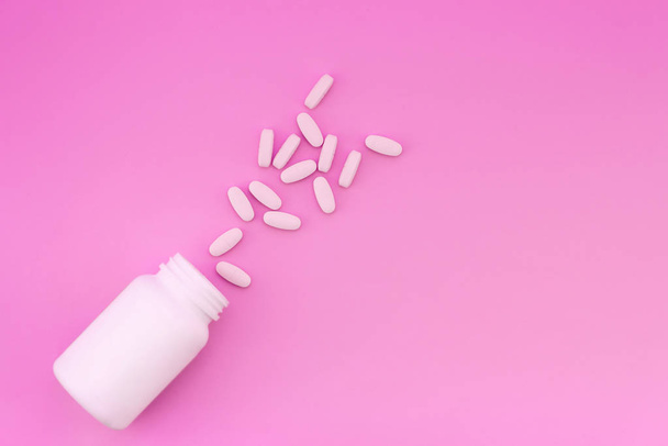 White tablets and a white bottle are isolated on a bright pink background. Medical concept - Fotó, kép
