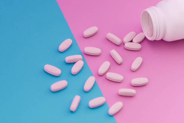 Macro Photo of white pills that pour out of a bottle on a bright blue and pink background. Medical concept - Fotó, kép