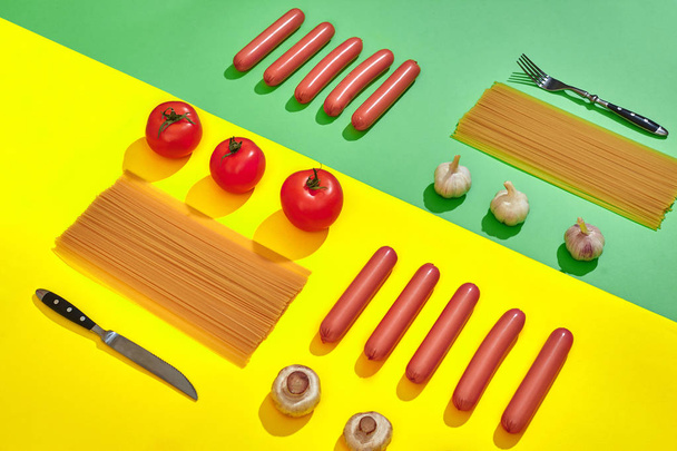 Sausages with tomatoes, mushrooms, spaghetti and garlic on a green and yellow minimal background. Flat lay. Top view. - 写真・画像
