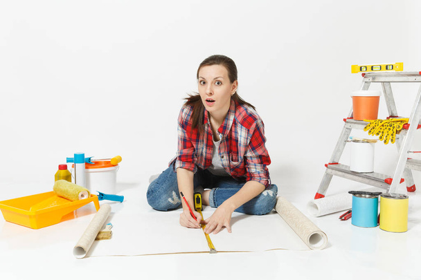 Woman sitting on floor with wallpaper rolls, measure tape, instruments for renovation apartment isolated on white background. Accessories for gluing, painting tools. Repair home concept. Copy space. - Photo, Image