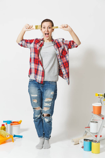 Full length portrait of fun cute woman with brush standing near instruments for renovation apartment home isolated on white background. Wallpaper accessories for gluing painting tools. Repair concept. - Photo, Image