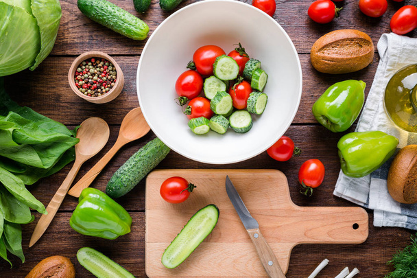Kochsalat, Gurken, Tomaten, Spinat auf einem Holztisch mit Schneidebrett - Foto, Bild